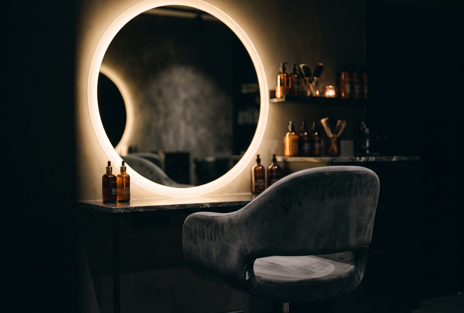 A high-end salon chair before a halo-lit mirror, glowing champagne gold in the dark.