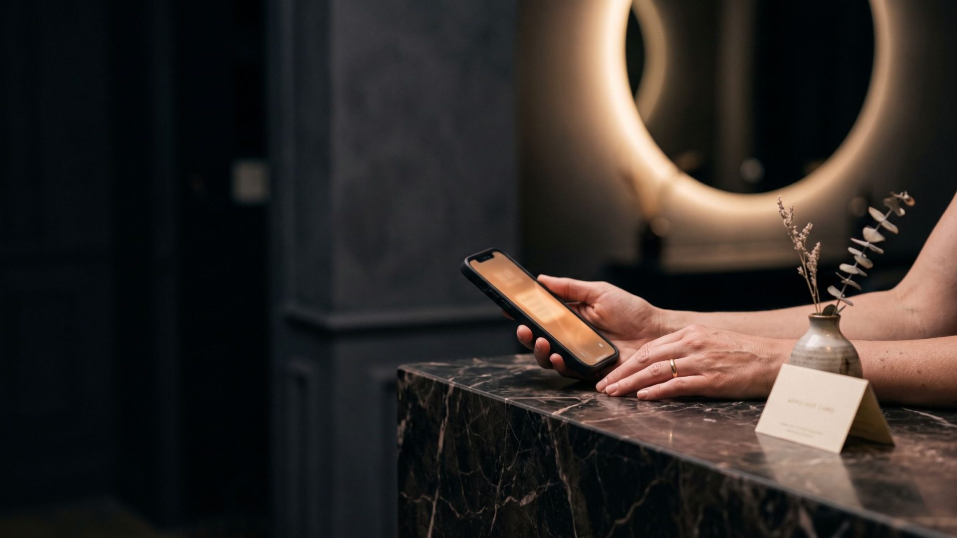 A woman books an appointment on her phone at a marble salon reception counter